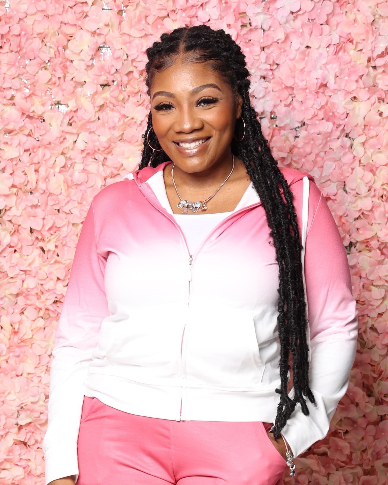 Tiffany Teasley smiling in a pink and white tracksuit against a wall of pink flowers.